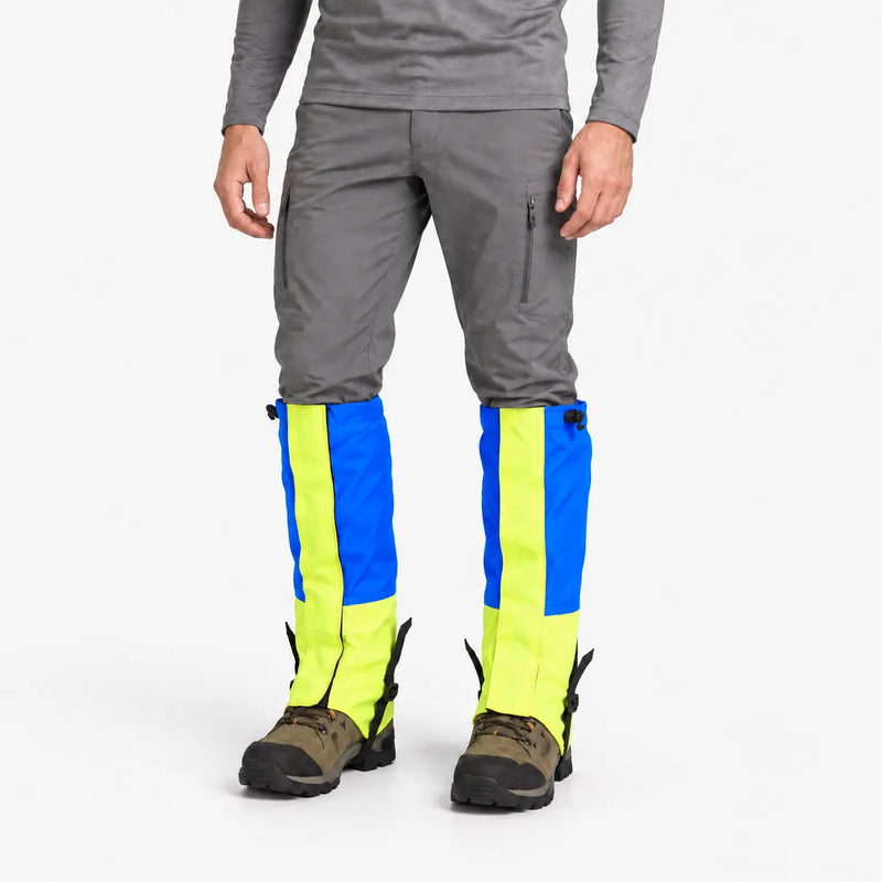 Model in grey trousers wearing blue and neon yellow gaiters over hiking boots, front view on white background 2