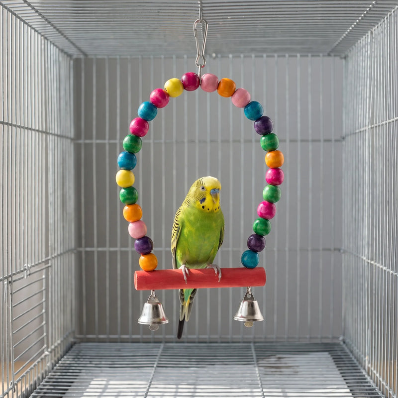 Budgerigar standing on the red wooden perch of the beaded arch swing, with two silver bells hanging below. 3