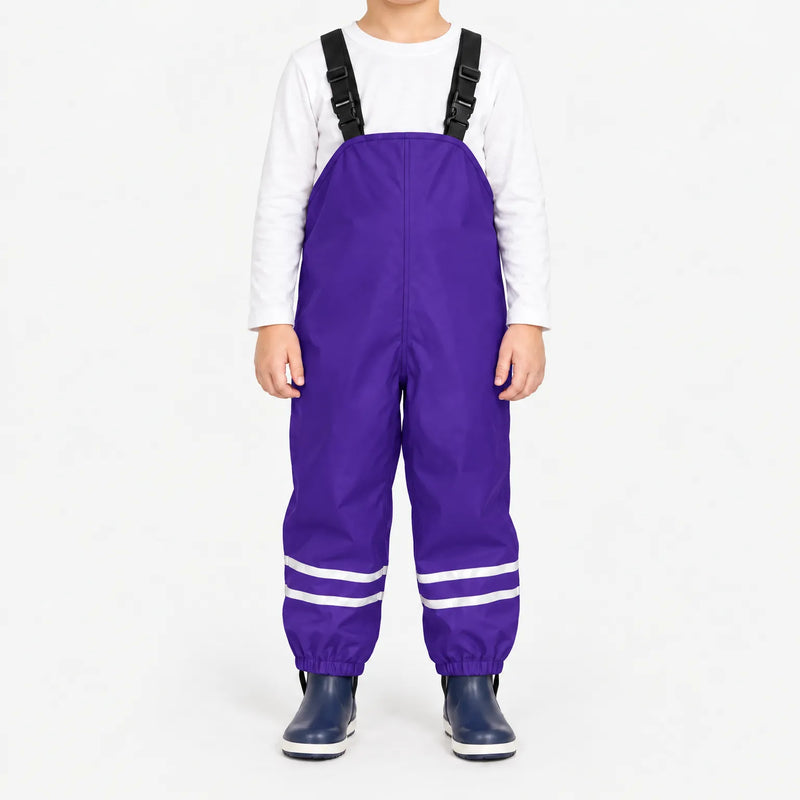 Child facing front in purple waterproof dungarees with adjustable black straps, reflective ankle stripes and navy boots, white background. 12