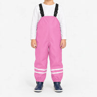Child facing front in light pink waterproof dungarees with black buckled straps, reflective leg stripes and navy boots, white background. 13