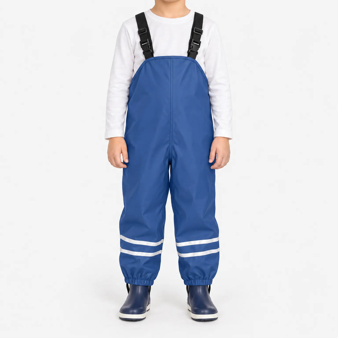 Child facing front in blue waterproof dungarees with adjustable black straps, reflective ankle stripes and navy boots against a white background. 2