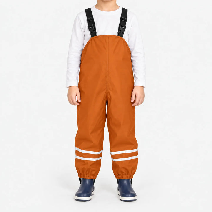 Child facing front in orange waterproof dungarees with black buckled straps, reflective leg stripes and navy boots, white background. 8