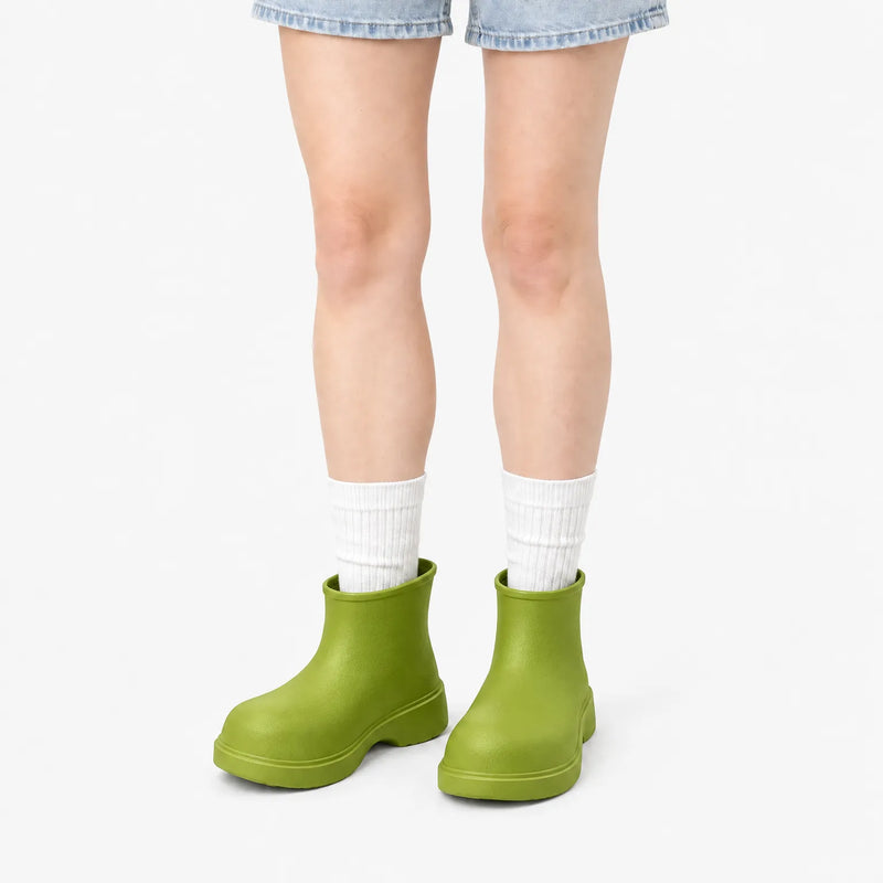 Olive-green ankle boots worn by a model in denim shorts and white ribbed socks against a plain white background. 10