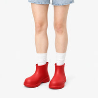 Bright red ankle boots worn by a model in denim shorts and white ribbed socks against a plain white background. 8