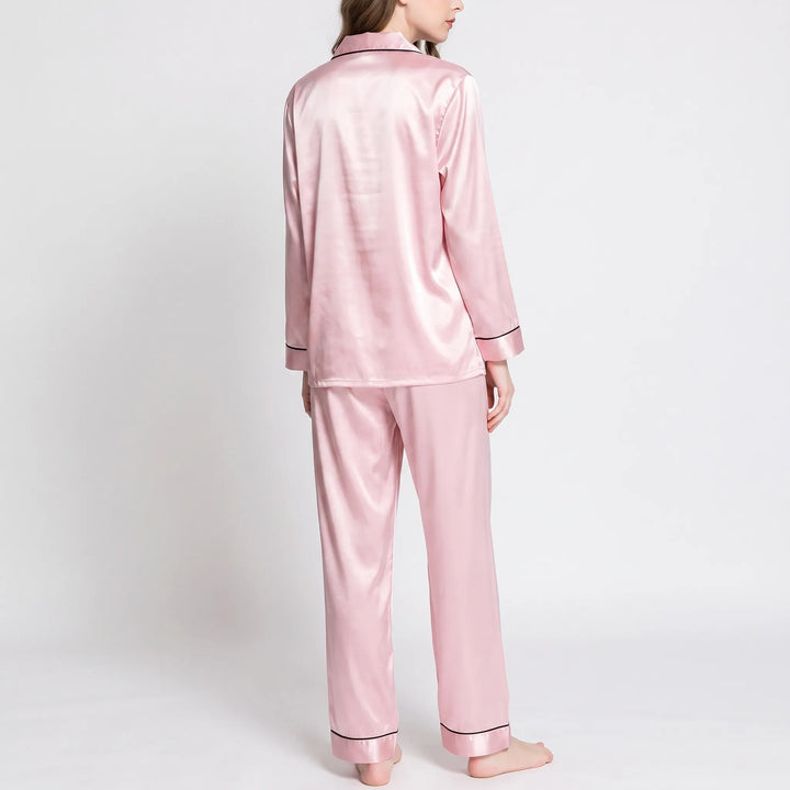 Back view of the pink satin pyjama set worn by a model, showing the smooth back and piped cuffs. 3