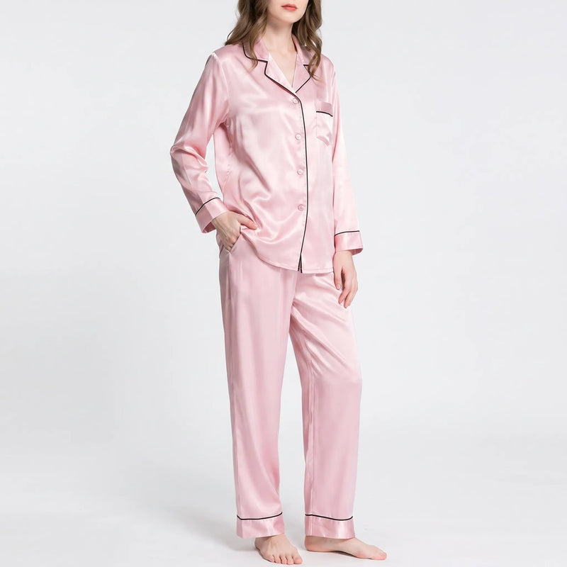 Model in the pink satin pyjamas with one hand in a trouser pocket, showing buttoned front and piped sleeve cuffs. 6