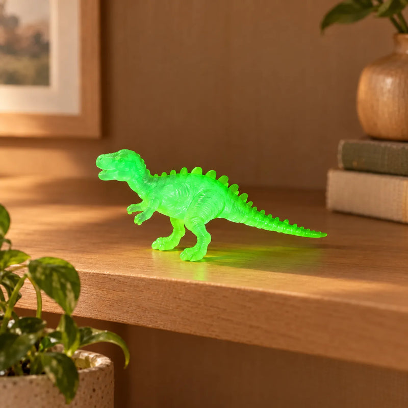 Single translucent bright green dinosaur figure with a spiny back standing on a wooden shelf beside a plant and a stack of books. 3