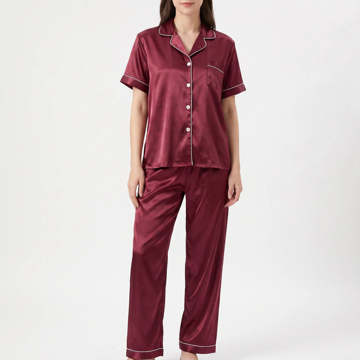 Front view of a model in the burgundy satin pyjama set, showing the button-up top, chest pocket and white piping. 2