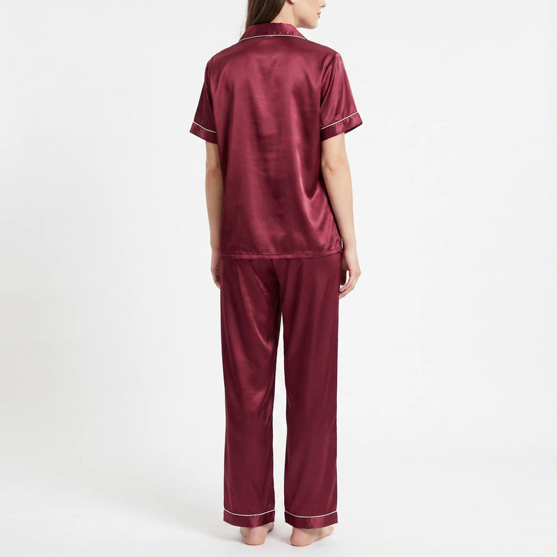 Back view of the burgundy satin pyjama set on a model, showing the plain back of the shirt and long trousers. 3