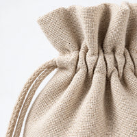Close-up of the woven beige linen texture, gathered drawstring top and braided cord of a single bag against a white background. 3