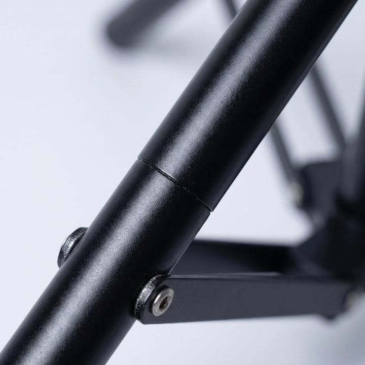 Close-up of a matt black tubular tripod leg with a metal joint, screws and a brace arm, softly blurred background. 3