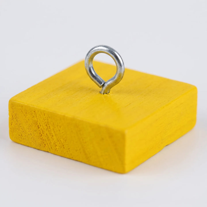 Close-up of a single yellow wooden block with a metal eye ring screwed into the top, showing the painted wood grain. 3