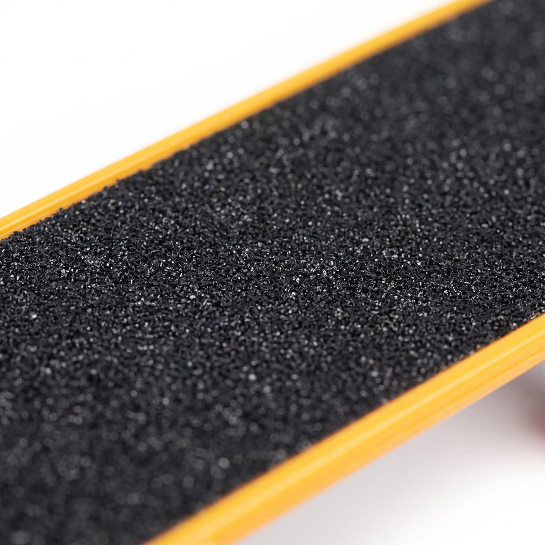 Close-up of the rough black grip surface on the skateboard deck, framed by a smooth orange edge. 3