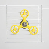 Front view of the yellow three-armed spinner toy fixed to white cage bars, with pearl beads in each ring. 1