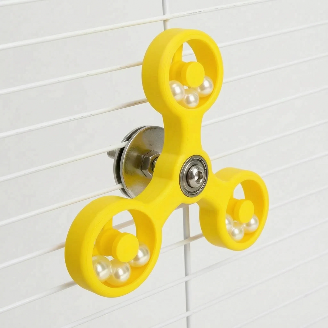 Yellow spinner toy seen at an angle on white cage bars, showing the washer and bolt fixing behind the arms. 7