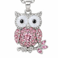 Close-up of an owl pendant necklace with large white eyes, a pink crystal body and a small pink-gem leaf branch. 4