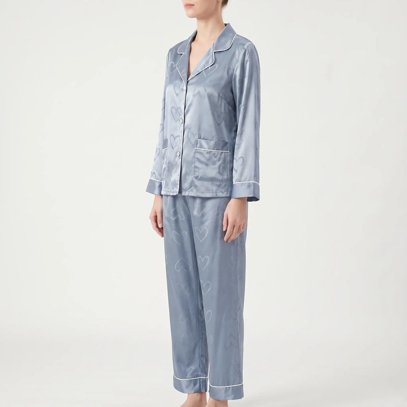 Three-quarter side view of the blue heart-patterned satin pyjamas on a model, showing a patch pocket and piped cuffs. 4