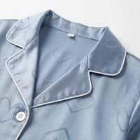 Close-up of the blue satin pyjama top's notched collar with white piping, a white button and the tonal heart pattern. 5