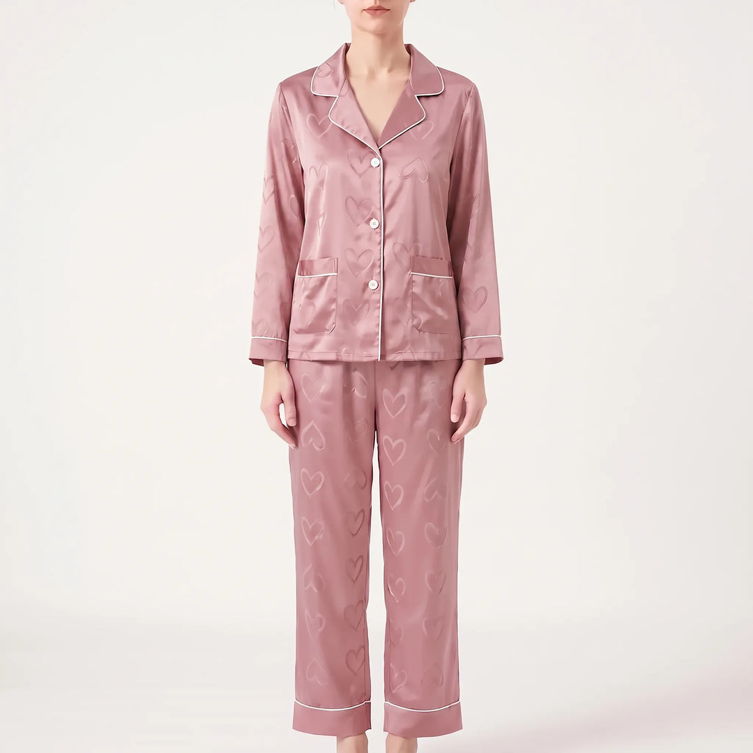 Model facing forward in the pink version of the satin pyjamas with heart pattern, white piping, buttons and two pockets. 6