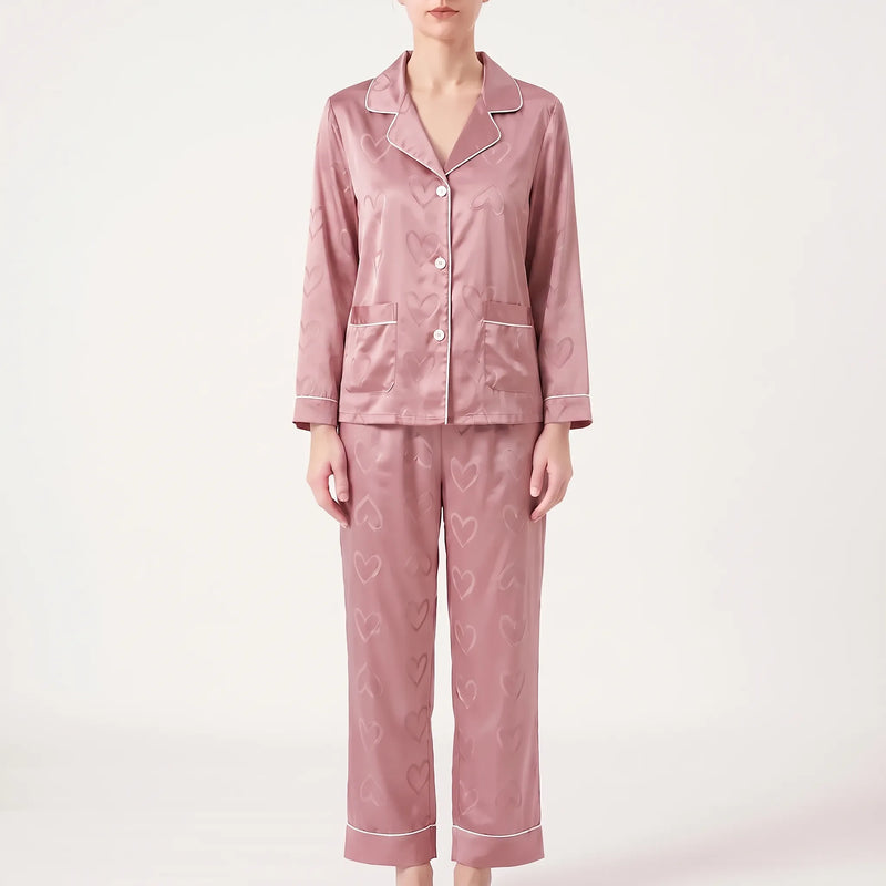 Model facing forward in the pink version of the satin pyjamas with heart pattern, white piping, buttons and two pockets. 6