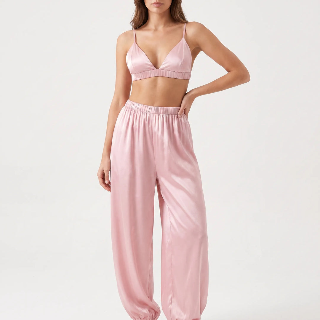Model with one hand on her hip in the pink satin bralette and gathered-waist jogger-style pants, studio front view. 2
