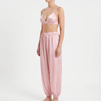 Three-quarter side view of the pink satin bralette and relaxed trousers with elasticated waist and ankle cuffs, worn by a model. 4