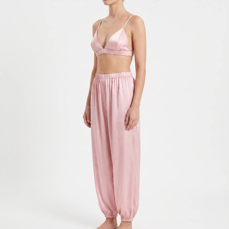 Three-quarter side view of the pink satin bralette and relaxed trousers with elasticated waist and ankle cuffs, worn by a model. 4
