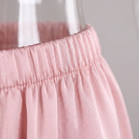 Close-up of the pink satin trousers' elasticated, gathered waistband with fine stitching, shown against a glass vase. 5