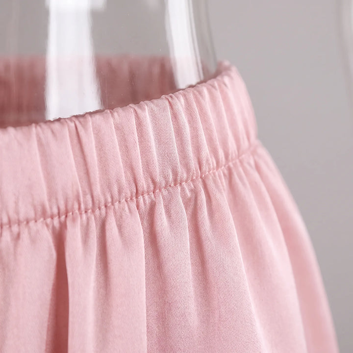 Close-up of the pink satin trousers' elasticated, gathered waistband with fine stitching, shown against a glass vase. 5