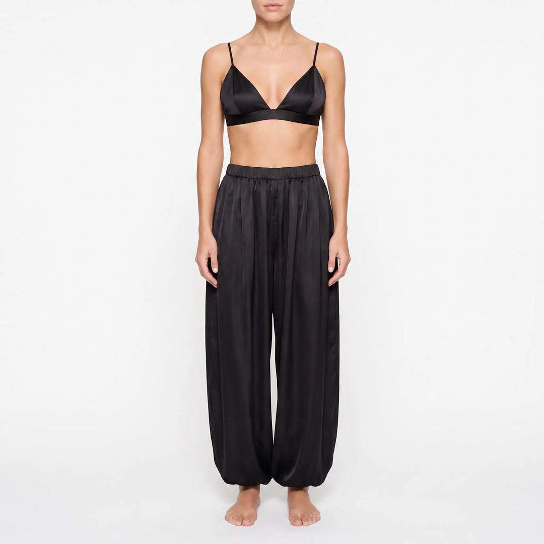 Model in the black satin version of the triangle bralette and wide balloon-leg trousers with elastic waist, front view. 6