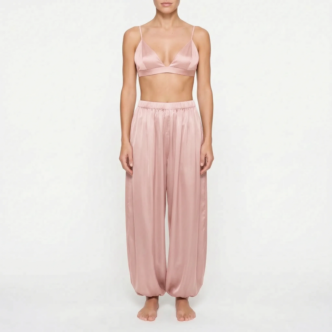 Model wearing the dusty rose satin version of the bralette and wide, gathered trousers, front view on a plain background. 7