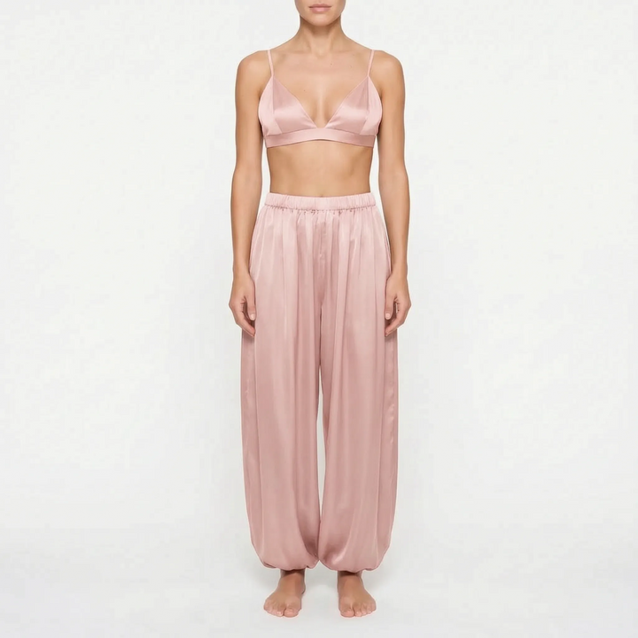 Model wearing the dusty rose satin version of the bralette and wide, gathered trousers, front view on a plain background. 7