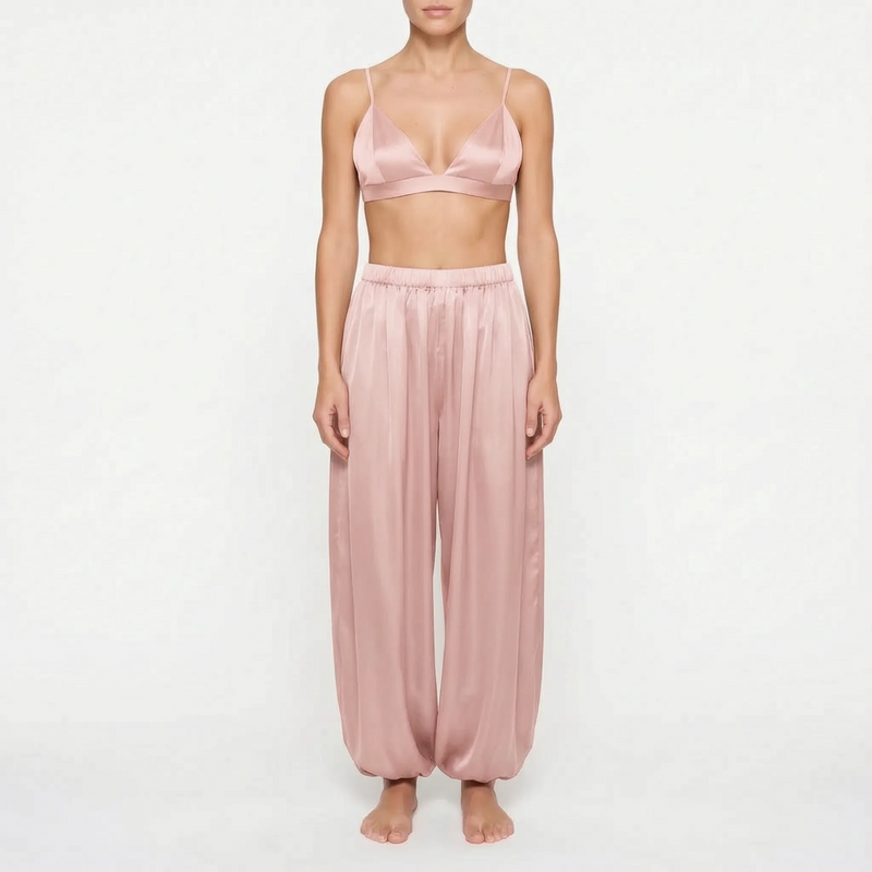 Model wearing the dusty rose satin version of the bralette and wide, gathered trousers, front view on a plain background. 7