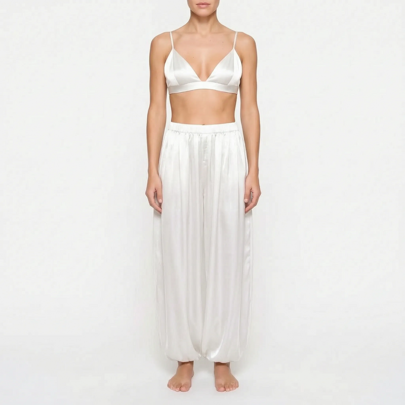 Model wearing the white satin version of the triangle bralette and full gathered trousers, front view on a plain background. 8