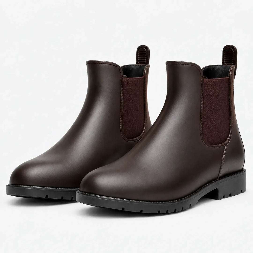 Pair of brown Chelsea rain boots with brown elastic panels, pull tabs and black treaded soles, shown at an angle on white. 7