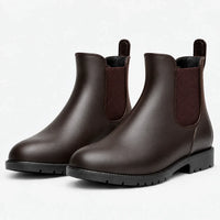 Pair of brown Chelsea rain boots with brown elastic panels, pull tabs and black treaded soles, shown at an angle on white. 7