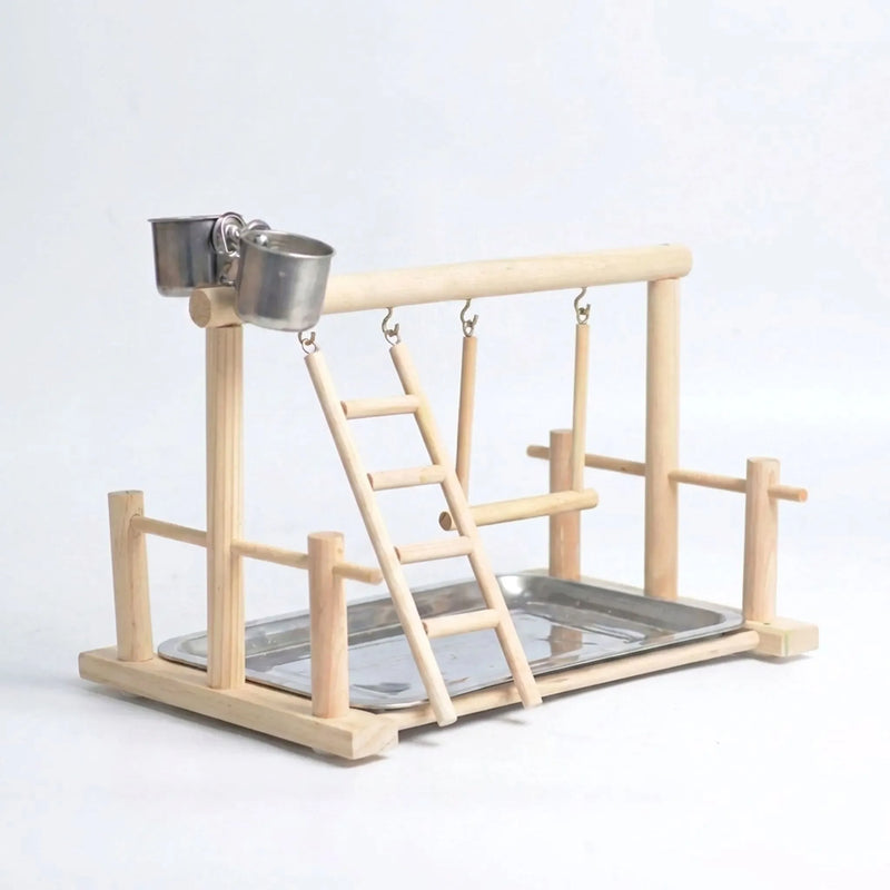 Empty natural wooden bird playstand on a plain pale background, showing the top perch, hanging ladder, swing, two steel cups and steel tray. 1