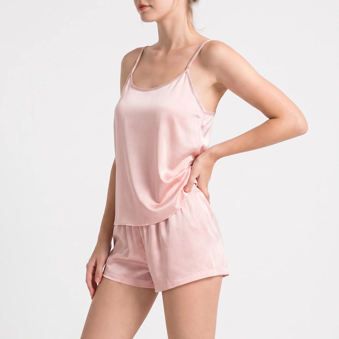 Three-quarter side view of the pale pink satin camisole and shorts, model with one hand on hip. 4