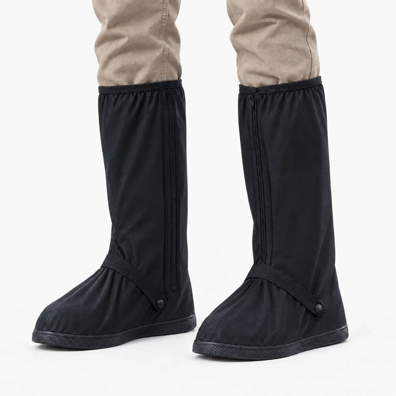 Front view of black tall shoe covers with front zippers and ankle straps worn over khaki trousers on a white background. 7