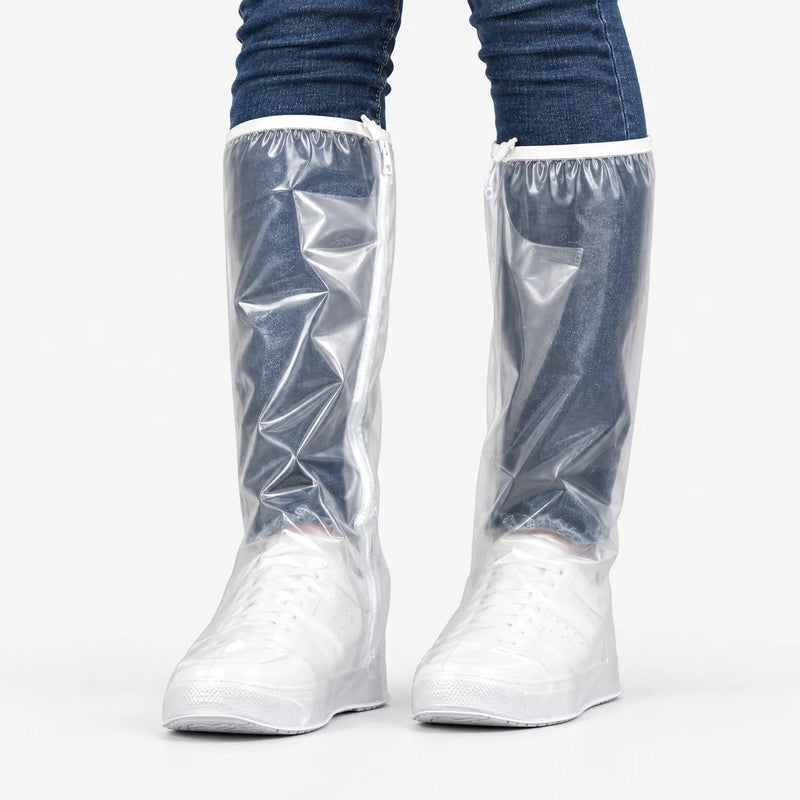 Front view of clear tall overshoes with a side zipper and white top trim, worn over white sneakers and jeans on a plain background. 2