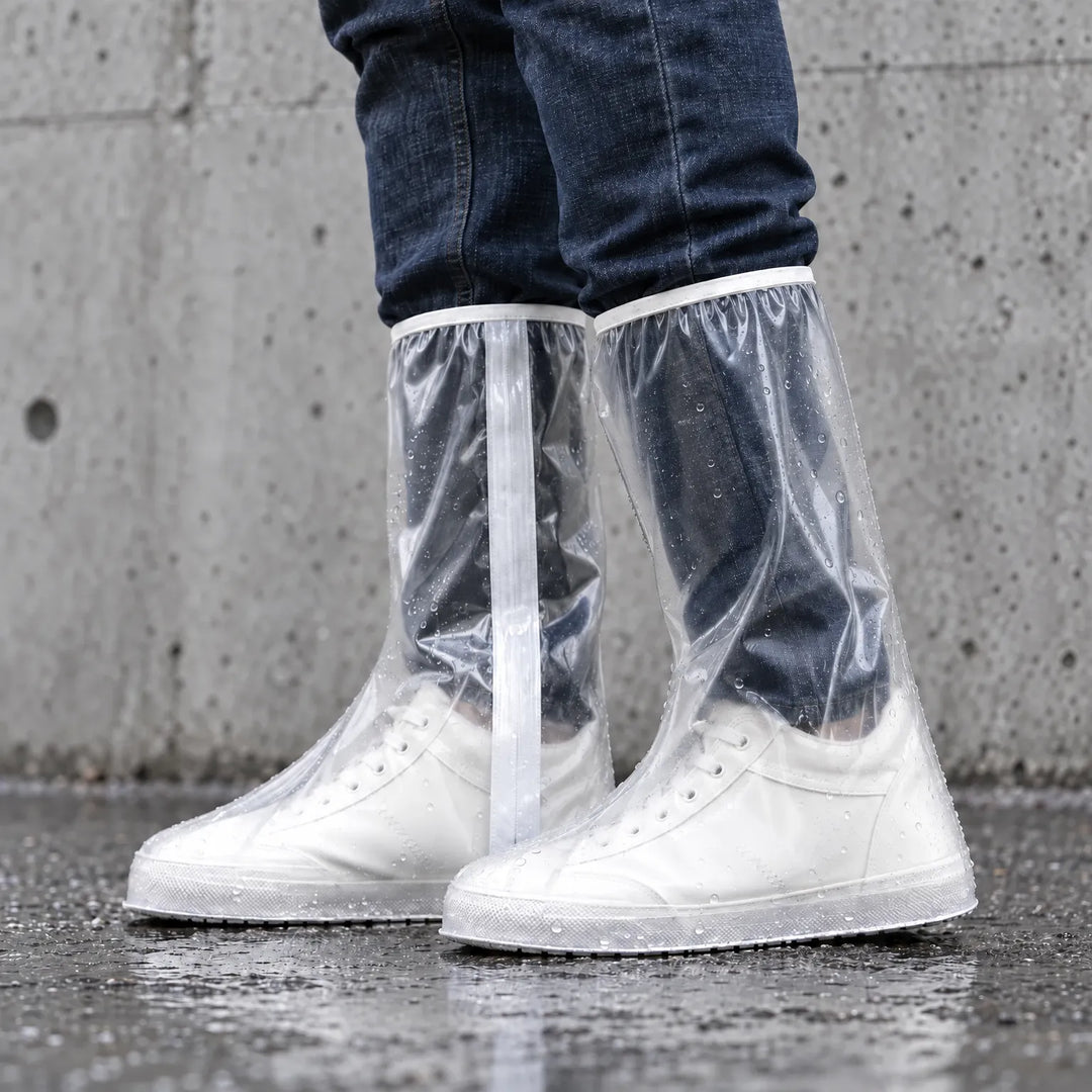 Side view of clear tall overshoes with a white strip along the leg, worn over white sneakers and dotted with raindrops against a concrete wall. 3
