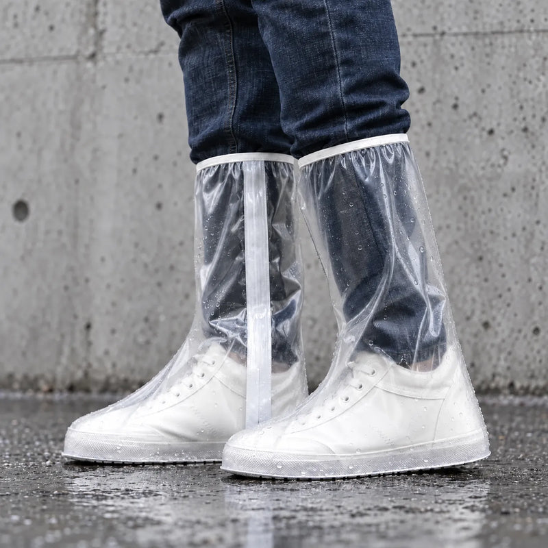 Side view of clear tall overshoes with a white strip along the leg, worn over white sneakers and dotted with raindrops against a concrete wall. 3