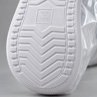 Close-up of the white rubber sole of an overshoe, showing its chevron tread pattern and ridged edge. 6