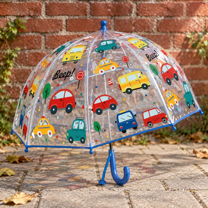 Clear dome umbrella with blue trim and handle, printed with colorful cars and buses, standing on paving stones in front of a brick wall. 3