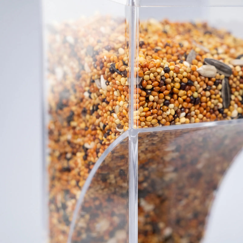 Close-up of the clear acrylic panels and curved chute, showing the mixed seed inside the feeder. 3