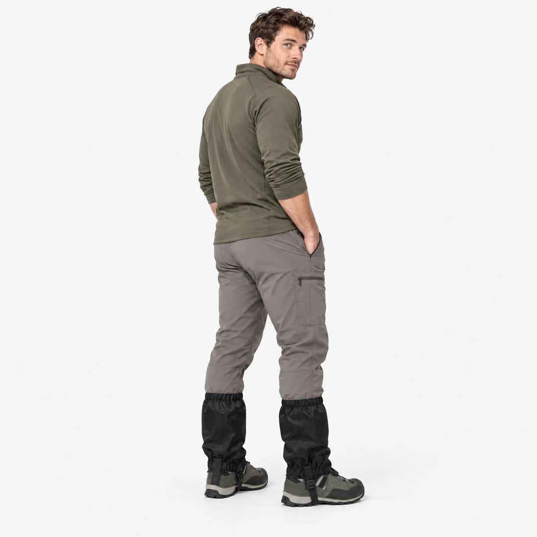 Man in a green long-sleeve top and grey trousers looks over his shoulder, wearing black gaiters over hiking boots. 4