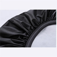 Close-up detail of the black cover's elasticated hem, gathered fabric and woven edging, over a pale grey surface. 6