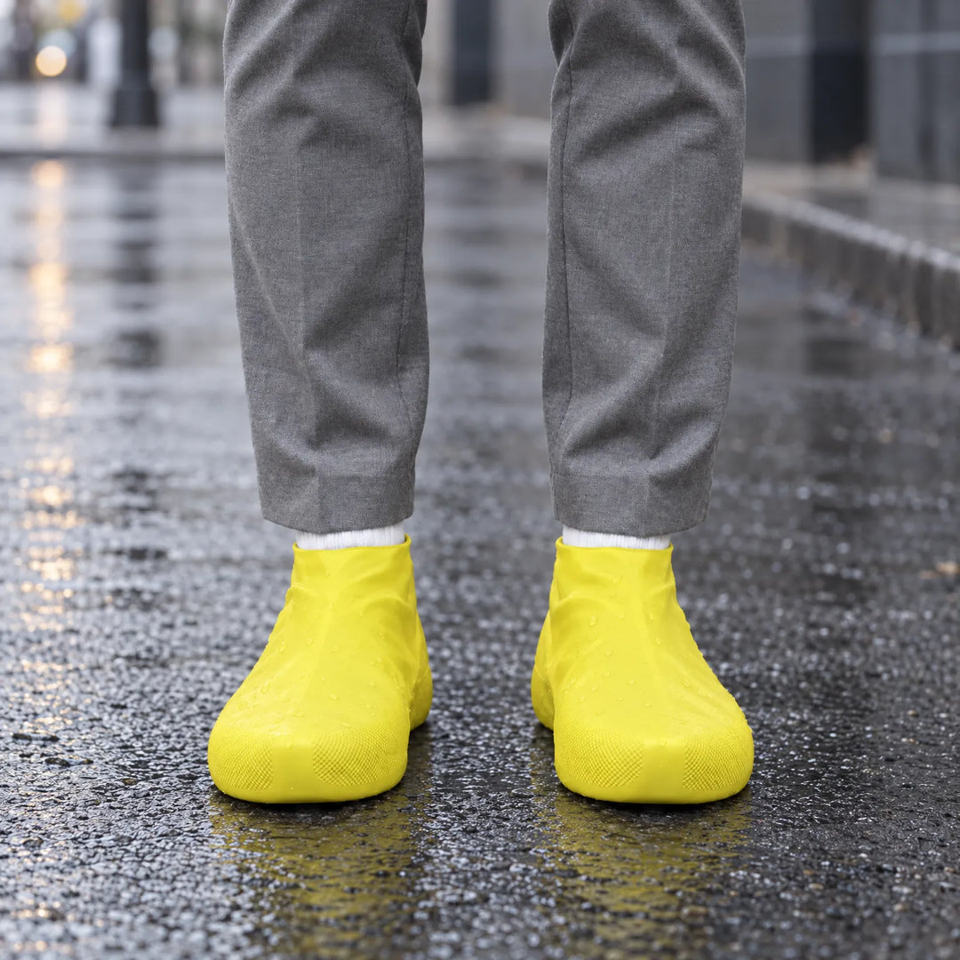 Yellow rubber shoe covers worn on a wet city street, with water droplets beading on the surface and a rainy backdrop. 3