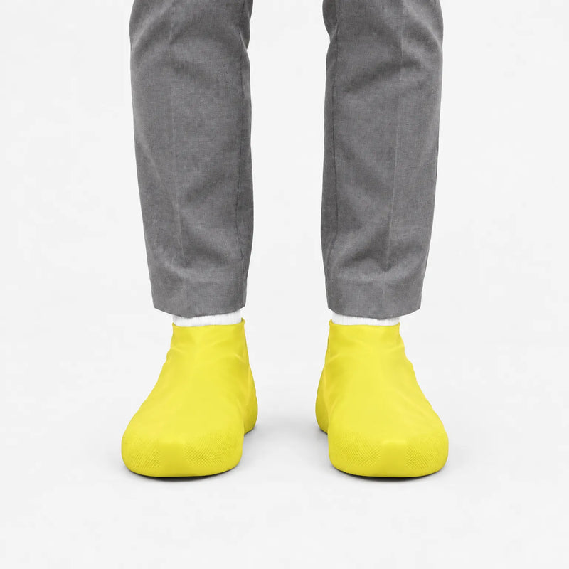 Front view of bright yellow rubber shoe covers worn with grey trousers and white socks against a plain white background. 7