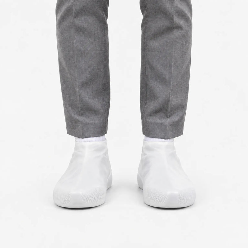 Front view of translucent white rubber shoe covers worn with grey trousers, with the grip texture visible on the toes. 8